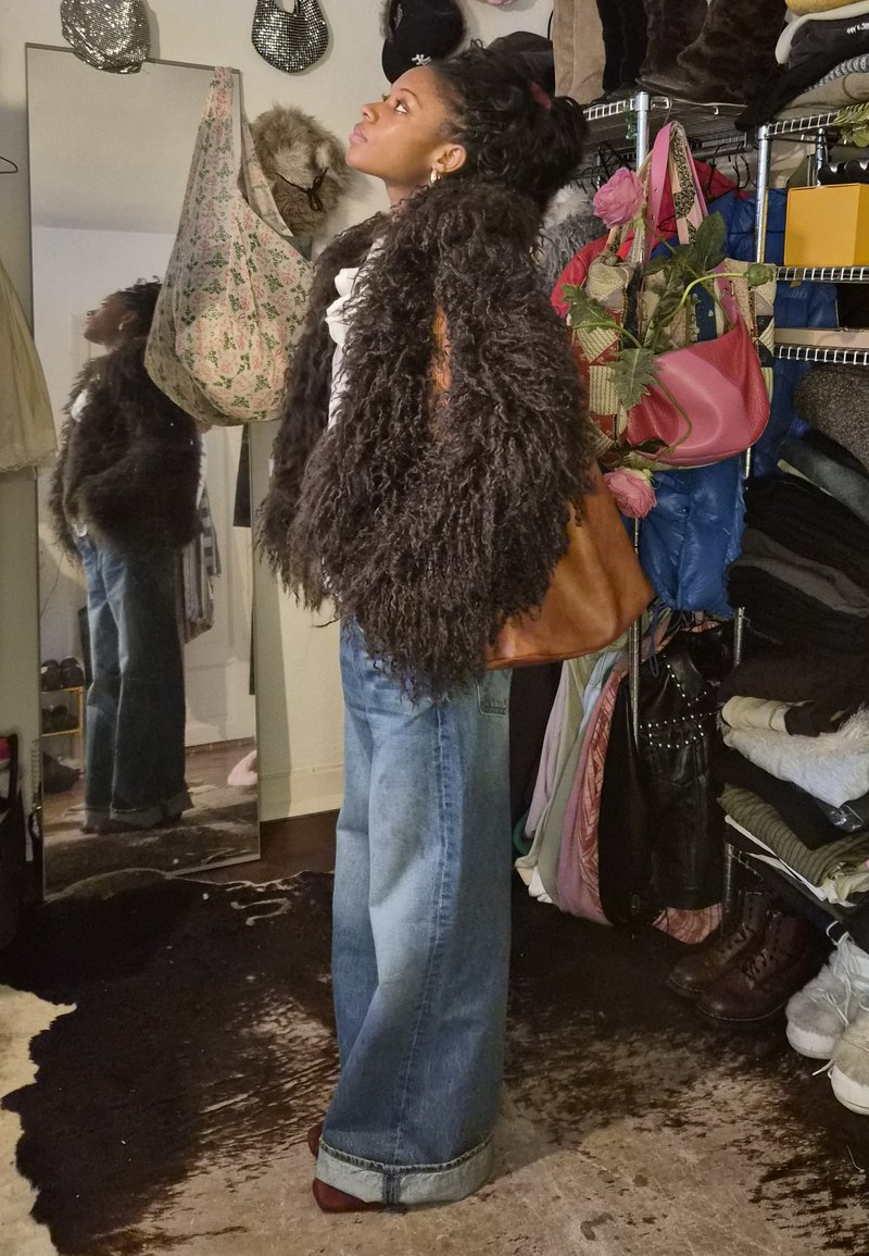 Furry brown coat, white top, and wide denim jeans. Accessories include a tan bag. Mirrored reflection visible. Closet background.