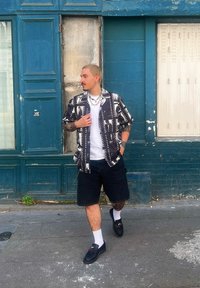 Μαύρο και άσπρο πουκαμίσo με μανίκια κοντά, άσπρη μπλούζα από μέσα, σκούρες βερμούδες, μαύρα παπούτσια και άσπρες κάλτσες που φοριούνται σε αστικό περιβάλλον.