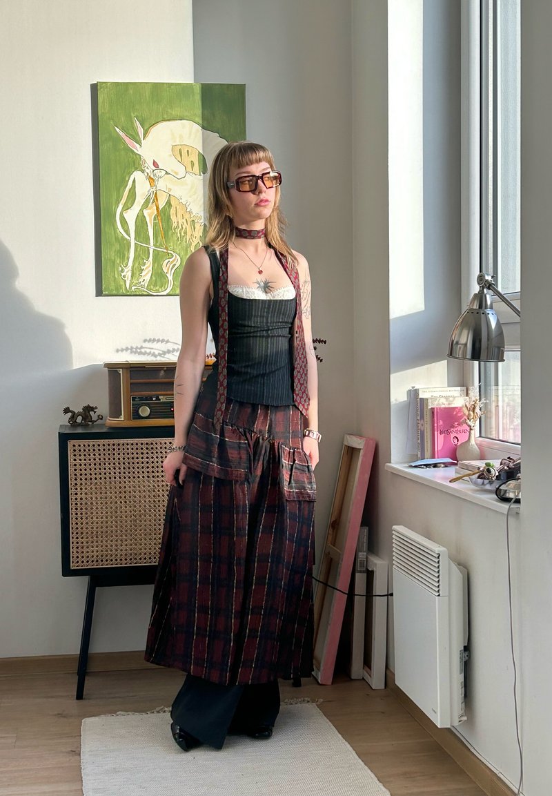Long plaid skirt in dark and light tones, layered over a fitted black top with a white lace edge. Accessories include sunglasses and a choker.