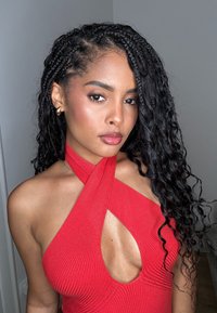 Top halter rojo acanalado con un diseño de escote en V profundo, que presenta tirantes cruzados y una silueta ajustada. El cabello rizado y los pendientes de oro completan el look.