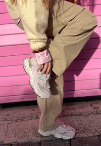Baskets New Balance rose clair avec détails en mesh et daim, semelle épaisse, et accents perle, portées avec un pantalon beige à jambes larges et un pull crème.