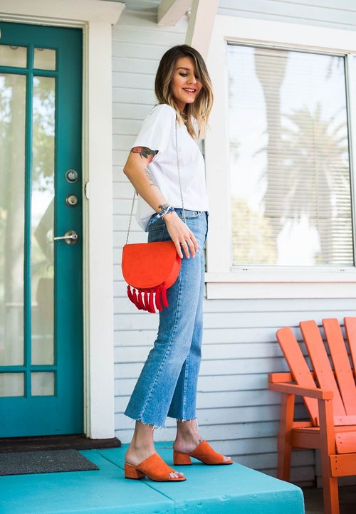 Fekete, bő szárú nadrág, sötétkék, gombos ing fehér szegélyezéssel, piros keresztpántos táska, kék magassarkú cipő, áll a köves utcán.