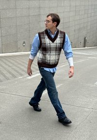 Veste à carreaux marron et blanc sur une chemise bleue, associée à un jean bleu et des chaussures noires, marchant sur une surface grise texturée.