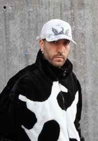 Juoda ir balta dirbtinio kailio striukė su karvės raštu ir aukšta apykakle; balta kepurė su erelio grafika ir siuvinėjimo detalėmis.