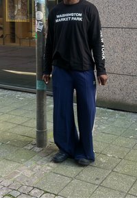 Μαύρη μακριά μπλούζα με εκτύπωση "WASHINGTON MARKET PARK", ναυτικές φαρδιές παντελόνες με λευκές και χρυσές λωρίδες στο πλάι, μαύρα αθλητικά παπούτσια.