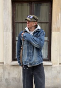 Jeanjacka i ljusblått med en urtvättad textur, lager på en grå huvtröja, i kombination med mörka baggyjeans och en brun axelväska.