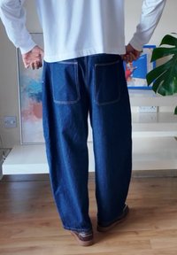 Spijkerbroek met een losse pasvorm, donkerblauwe kleur en opvallende stiksels. Voorzien van twee achterzakken en een rechte pijp, gecombineerd met bruine schoenen.