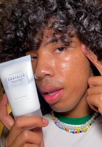 Λευκό σωληνάριο Κρέμας Σαμπουάν SKIN1004 Madagascar Centella Tone Brightening, κρατημένο στο χέρι, με κείμενο στην πρόσοψη και ορατό πολύχρωμο κολιέ από χάντρες.