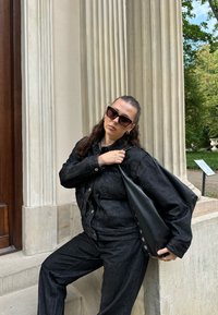 Must värviline teksajakk ja püksid nuppudega, millele on lisatud suur must nahkrahakott. Üks suur must päikeseprillide paar täiendavad välimust.