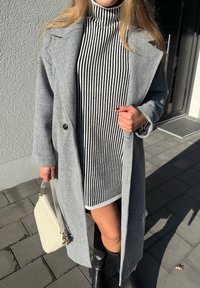 Palton gri din lână cu un singur nasture, purtat peste o rochie cu guler înalt în dungi alb-negru. Accesorizat cu o geantă deschisă la culoare și cizme până la genunchi.