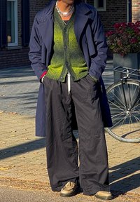 Ναυτική παλτό πάνω από ένα πράσινο gradient καζάκα, μαύρο παντελόνι σε φαρδιά γραμμή και μπεζ παπούτσια. Ασημένια αλυσίδα στο λαιμό και κουμπιά στα μανίκια του καζάκου.