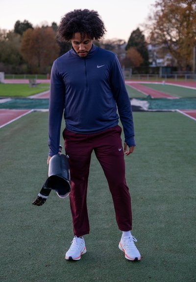 Hombre con ropa deportiva sosteniendo una pierna protésica de pie en un campo deportivo al aire libre durante el otoño.