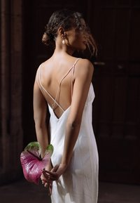 Valge siidiste rindadega kleit avatud seljaga, mida hoiab figuur, kes hoiab suurt roosat anthuriumõit. Sujuv tekstuur ja elegantne disain.