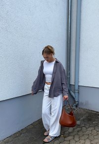 Siva lanena srajca čez belo kratko majico, bele široke hlače in rjava usnjena torbica. Sandali s sivimi trakovi dopolnjujejo obleko.