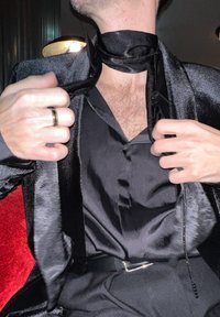 Chemise en satin noir et blazer à fini brillant. Le blazer possède un col châle et une écharpe noire en satin nouée autour du cou.