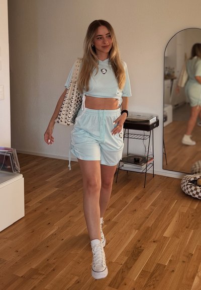 Top deportivo corto de color azul claro con tejido texturizado y logo, combinado con pantalones cortos a juego. Zapatillas altas blancas y un bolso con tachuelas.