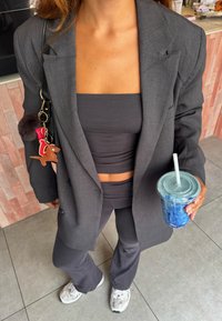 Grå blazer over en matchende crop-top og høy midje flared bukser, holder en blå drink i en klar kopp med sugerør.