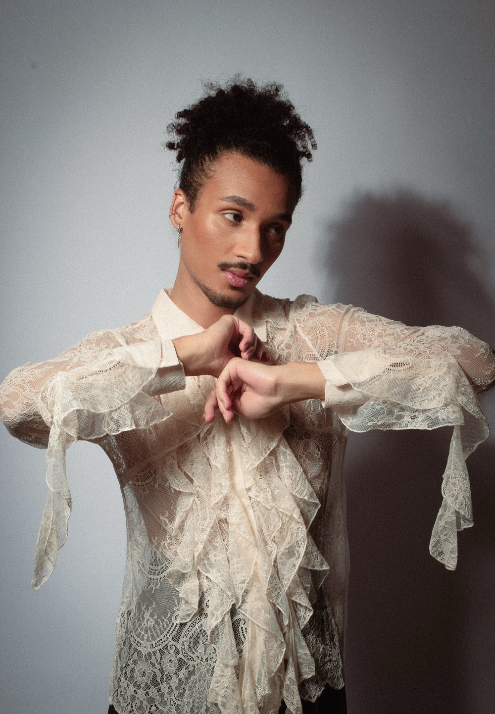 Blouse en dentelle avec des détails à volants, présentant des manches longues et évasées dans une douce couleur beige. Motifs floraux délicats sur l'ensemble.