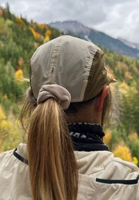 Jasnobezowy kapelusz o półprzezroczystej teksturze, związany koński ogon ozdobiony beżowym scrunchie, czarny komin na szyję i kremowa kurtka.