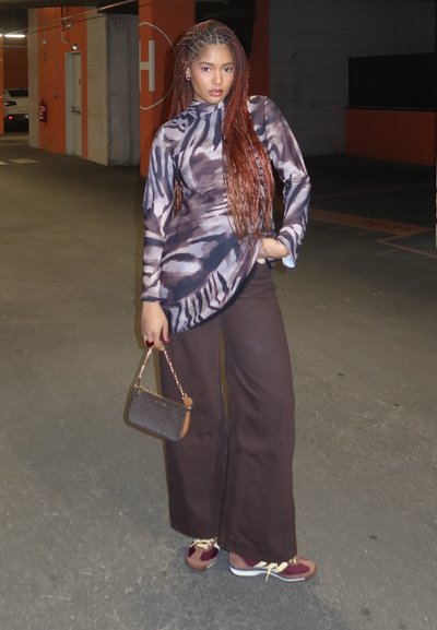 Top de manga larga ajustado con un patrón abstracto en marrón y gris, combinado con pantalones anchos marrones y zapatillas burdeos. Accesorio: bolso pequeño.