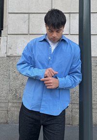 Camicia azzurro chiaro in cotone con maniche lunghe, collo piegato e vestibilità comoda. Abbinata a jeans in denim scuro.