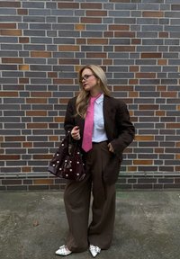 Hnedý károvaný oversize blejzer, biela košeľa, ružová kravata, hnedé široké nohavice, burgundská taška so striebornými cvočkami, biele špicaté topánky.