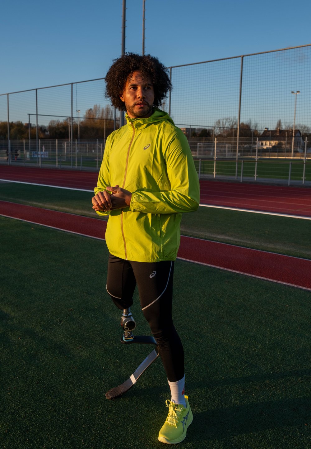 Atleta con una chaqueta ligera de color amarillo brillante, leggings deportivos negros y zapatos de neón amarillo, mostrando una pierna artificial con una cuchilla.