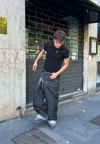 Vide baggy mørke denimjeans med opprevne sømmer, brukt med en svart tettsittende t-skjorte og grå fottøy. Tilbehør inkluderer nøkkelringer på et belte.