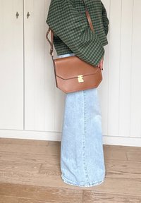 Koňakovo hnedá kožená kabelka so zlatými kovovými doplnkami a geometrickým tvarom. Nosená so zeleným károvaným sakom a svetlomodrou rifľovou sukňou.