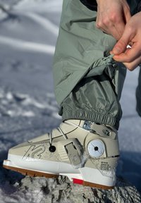 Bota de snowboard K2 em bege com sola branca e detalhes em vermelho, apresentando um upper texturizado, hardware ajustável e calcanhar reforçado.