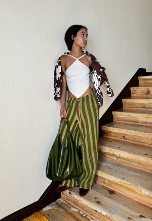 Top blanco sin mangas con dobladillo en punta, chaqueta de flores en tonos marrón y blanco de gran tamaño, pantalones sueltos a rayas verdes, bolso grande verde y zapatos burdeos.