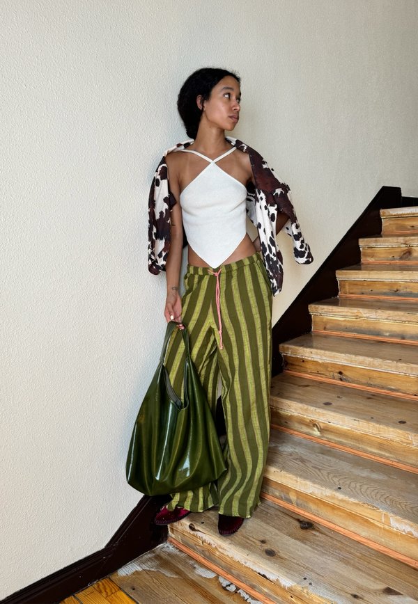 Top bianco con scollo a halter e orlo a punta, giacca oversize con stampa floreale marrone e bianca, pantaloni verdi a righe larghi, grande borsa verde e scarpe borgogna.