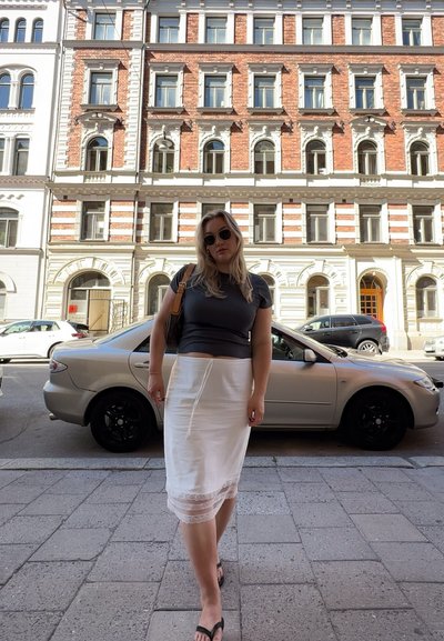 Falda lápiz blanca hasta la rodilla con encaje, combinada con una blusa gris ajustada. Unas gafas de sol negras y un bolso de hombro completan el conjunto.