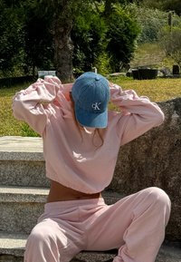 Lichtroze cropped sweatshirt en bijpassende sweatpants, gemaakt van gladde stof, met elastische boorden en tailleband. Blauwe denimpet met logo.
