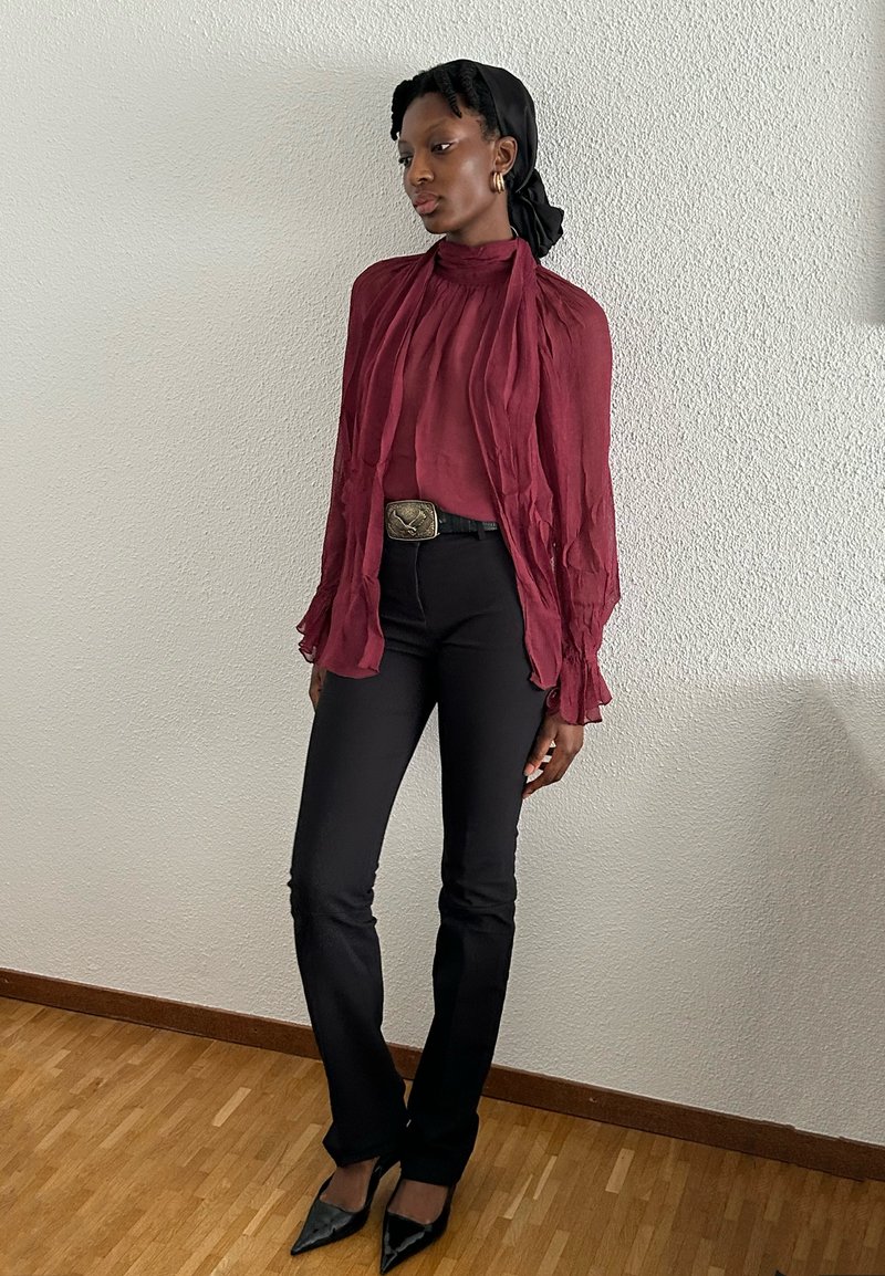 Maroon, textured blouse with ruffled sleeves, paired with fitted black pants and pointed black heels. Silver-buckled belt accentuates waist.
