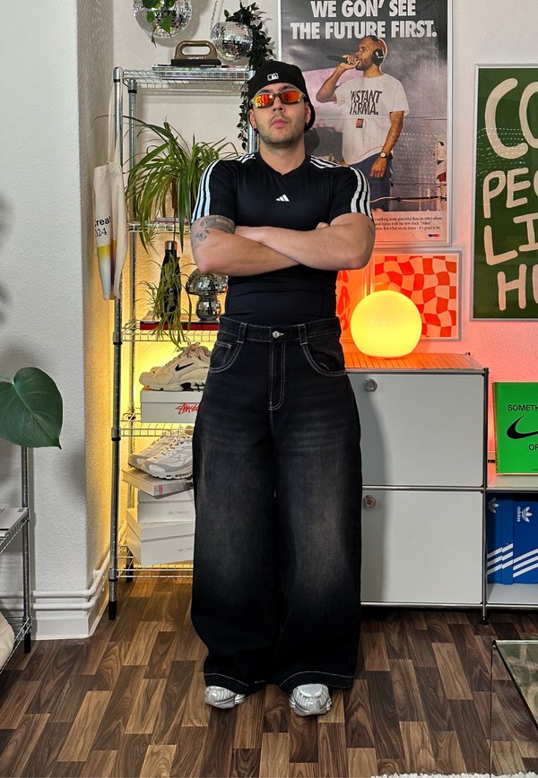 Laza fekete farmernadrág világos varrási részletekkel, fekete, testhezálló pólóval, amelynek ujjain fehér csíkok vannak. Ezüst sneaker.