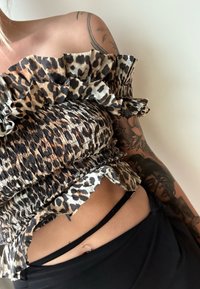 Top com padrão de leopardo, com um design de ombros à mostra em camadas, textura franzida e alças pretas de destaque. O material parece leve e texturizado.