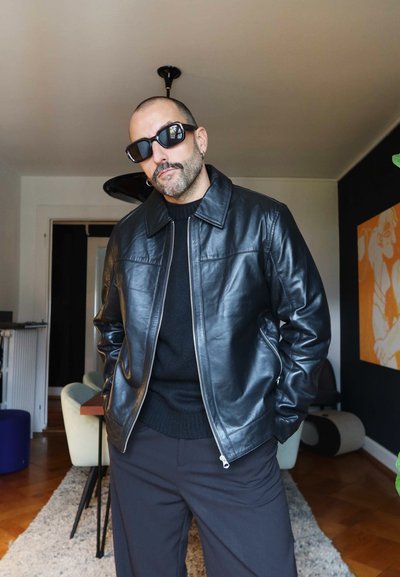 Chaqueta de cuero negra con cierre de cremallera, cuello y dos bolsillos laterales. Lleva puesta sobre un suéter negro y combinada con pantalones oscuros.