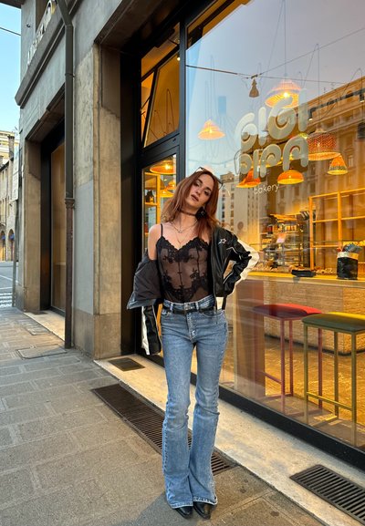 Body de encaje negro superpuesto a una chaqueta blanca y negra, combinado con jeans acampanados azules y tacones negros; fondo de tienda con luces colgantes.