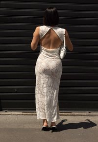 Biała koronkowa sukienka z wycięciem na plecach, dopasowana, długa do ziemi. W zestawieniu z małą białą torebką i czarnymi butami na obcasie.