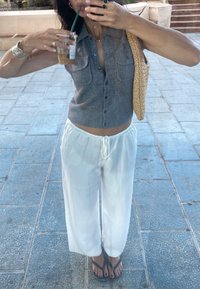 Grå cardigan med korte ærmer, knapdetaljer og to lommer, sammen med hvide, løsthængende bukser og sorte flip-flops, mens der holdes en drink.