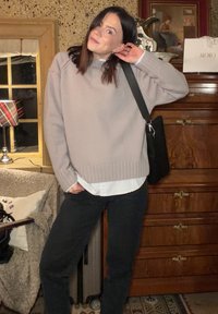 Pull en laine gris clair avec ourlet côtelé, superposé à une chemise blanche à rayures, associé à un pantalon foncé et un sac à bandoulière noir.