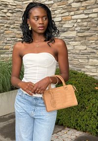 Handtas in bruin met krokodillenprint, rechthoekig van vorm, met bovenhandvatten en ritssluiting, getoond bij een neutrale outfit.