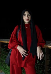 Piros kötött pulóver és hozzá illő nadrág, fekete kendővel párosítva. Egyszínű, laza fit, és egy keresztpántos táska. Éjjeli környezet.