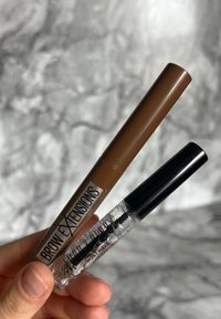 Zwei kosmetische Produkte: ein brauner Augenbrauenstift mit abgerundeter Spitze und ein transparenter Augenbrauengel mit einem schwarzen Applikator.