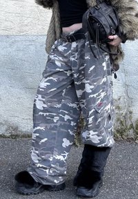 Pantalon cargo camouflage gris avec une taille élastique, doté de poches latérales et d'un patch logo rouge, associé à des bottes noires ornées de fourrure.