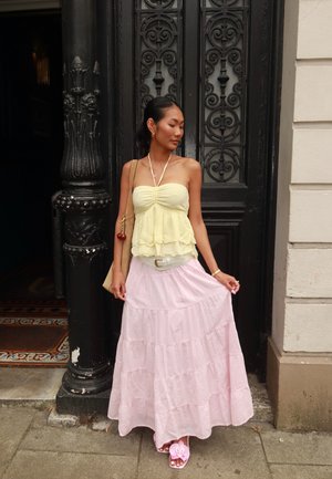 Blusa amarilla con capas y tirantes finos, combinada con una falda maxi de capas en rosa claro, accessorios con un cinturón blanco y sandalias con flores.