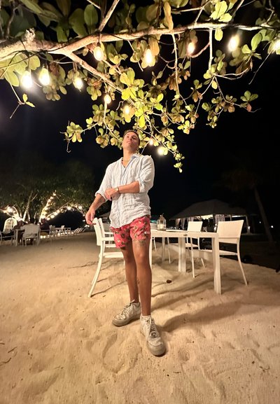 Conjunto casual que incluye una camisa azul claro, pantalones cortos florales y zapatillas blancas. Un árbol con luces en la parte superior crea una atmósfera cálida.