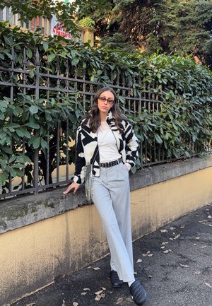 Chaqueta de piel con un patrón en blanco y negro sobre una camiseta blanca, combinada con pantalones de pierna ancha de rayas claras y zapatos negros sin cordones.