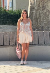 Blommönstrad, lätt tyg topp med spaghettistlån, parat med en lager-puffig krämfärgad kjol. Rosa handväska med fransdetalj. Grå plattformsskor.